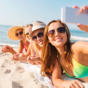 group of smiling women with smartphone on beach